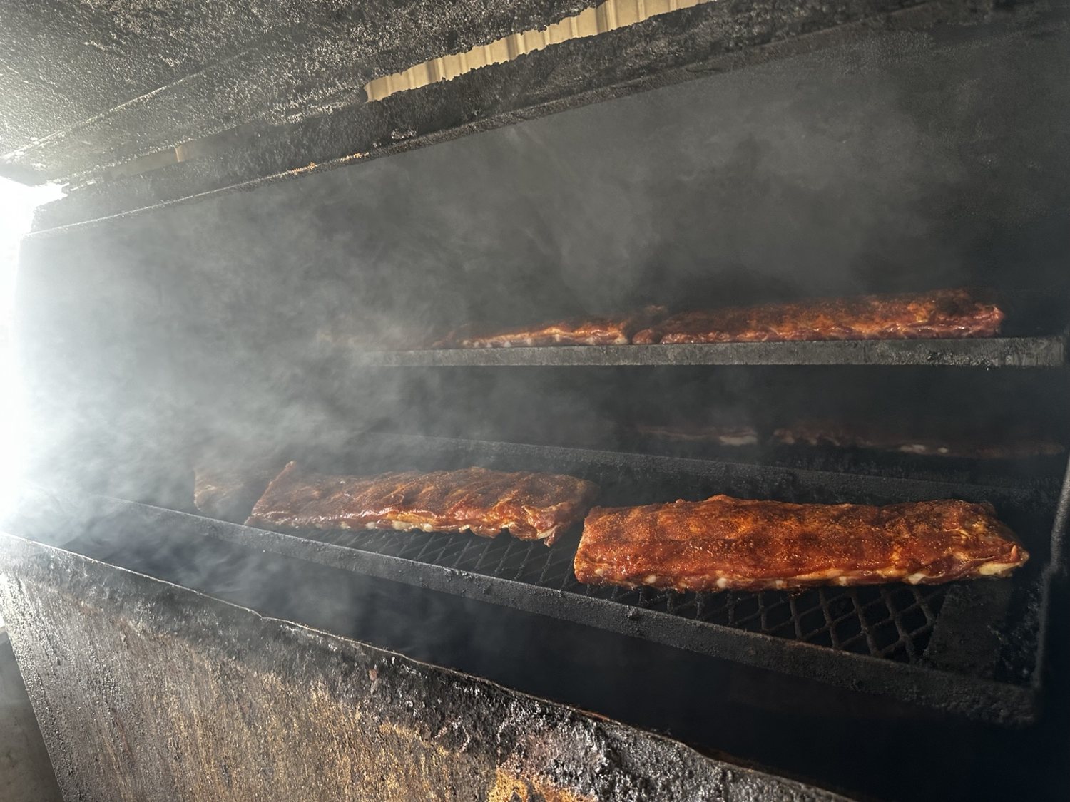 Racks of ribs cooking inside a smoky pit