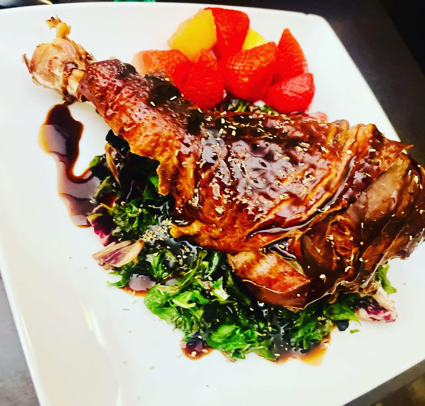 Roasted poultry over greens with fruit and a dark glaze